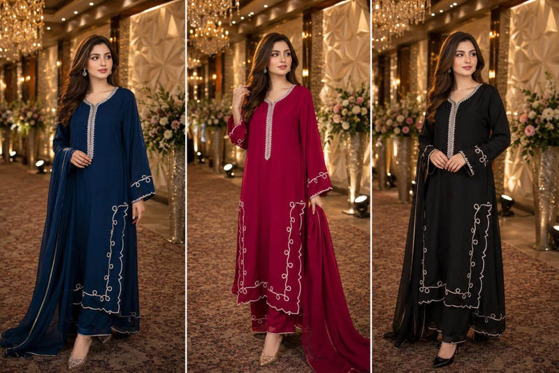 Three women modeling traditional South Asian salwar kameez sets in a grand indoor event hall with warm chandeliers and floral decor. The left set is navy blue, the center set is deep maroon, and the right set is black, each with white embroidered detailing on the neckline and borders.