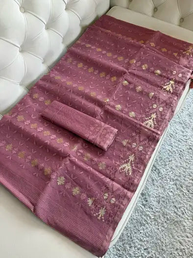 A folded and unfolded  rose pink saree with gold floral patterns, draped on a white tufted sofa next to a gray shag rug.