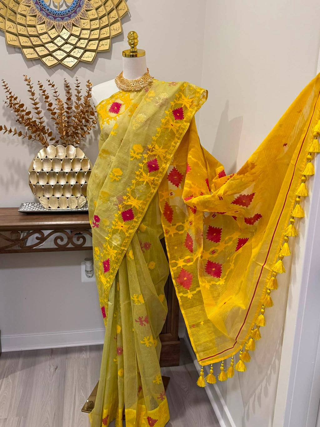 A yellow and green saree with red floral embroidery and yellow tassels, displayed on a mannequin in an indoor setting.