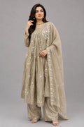 A woman modeling a traditional beige embroidered kurta set with matching wide-leg pants and a sheer dupatta, photographed against a solid gray studio background.