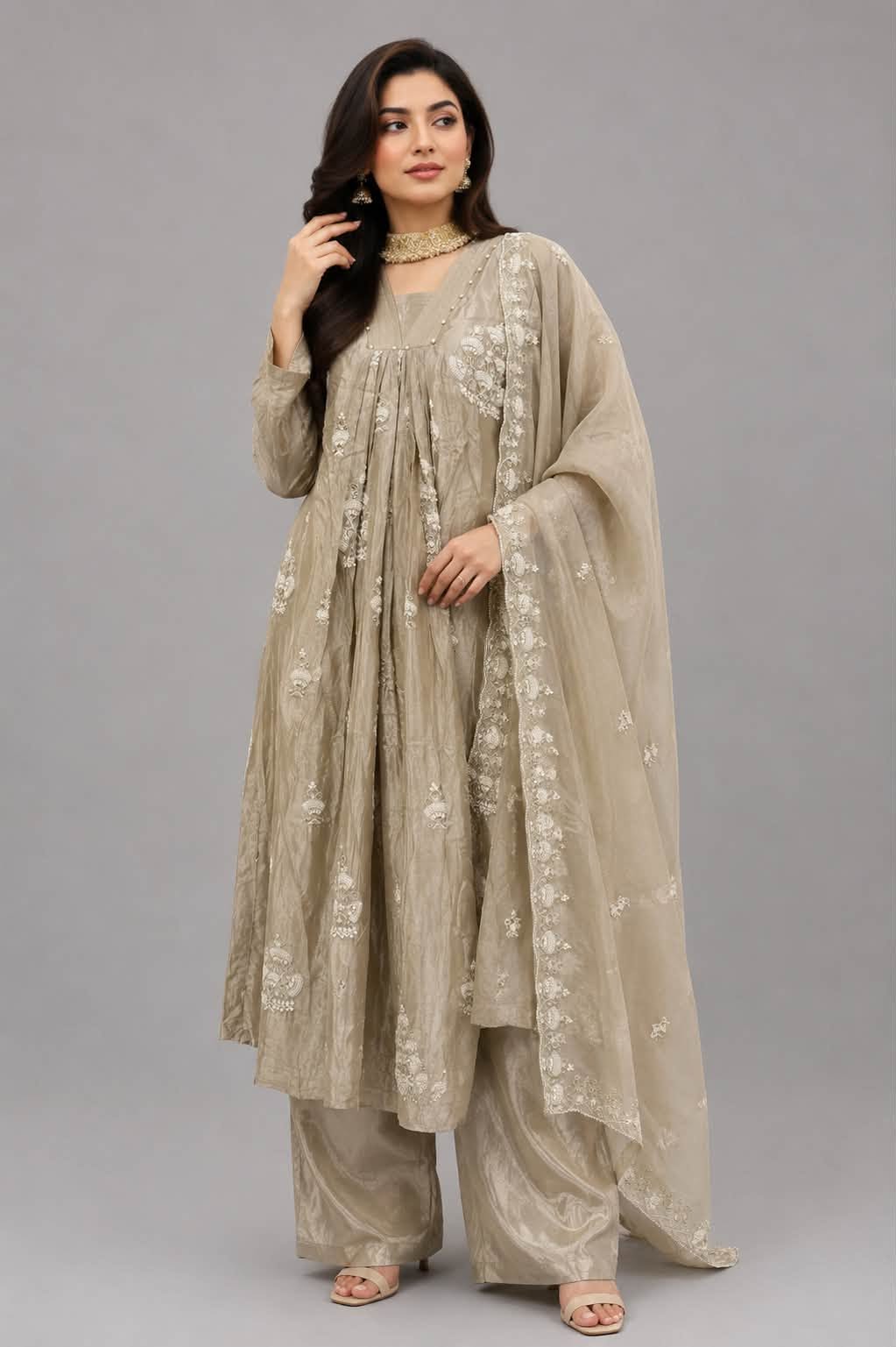 A woman modeling a traditional beige embroidered kurta set with matching wide-leg pants and a sheer dupatta, photographed against a solid gray studio background.