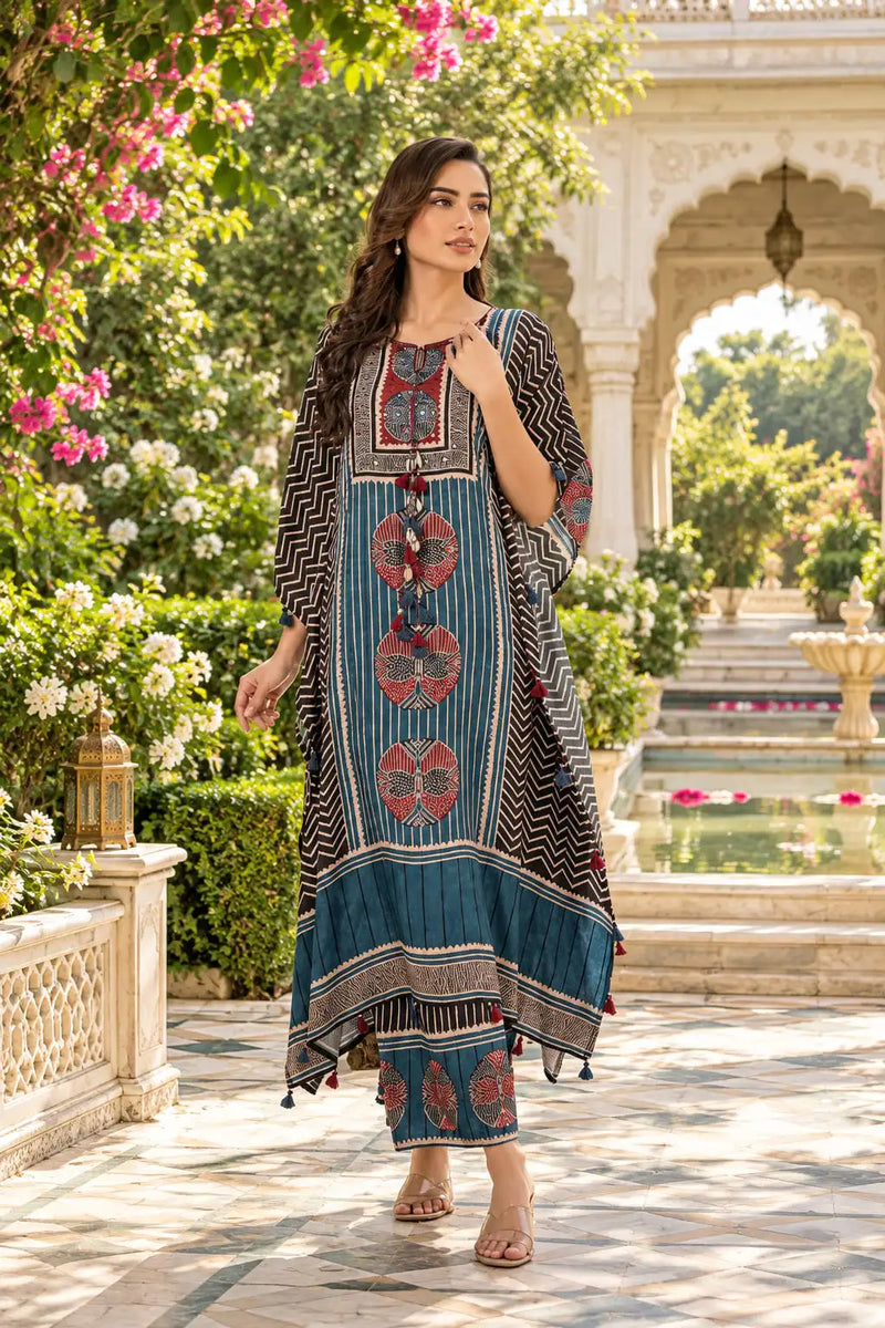 A woman models a traditional Indian kurta set in an outdoor courtyard setting. The kurta features a blue base with vertical stripes, red floral motifs, and black-and-white geometric patterns on the sleeves and border.